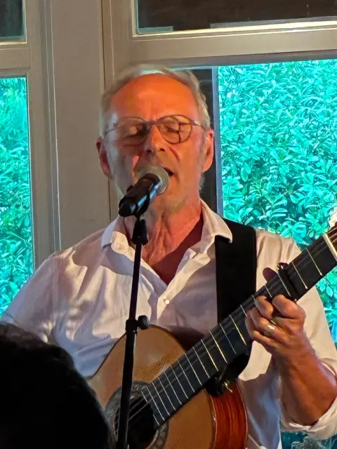 Reinhold Beckmann singt mit Gitarre am Mikrofon beim Sommer-BBQ in der Elb-Lodge